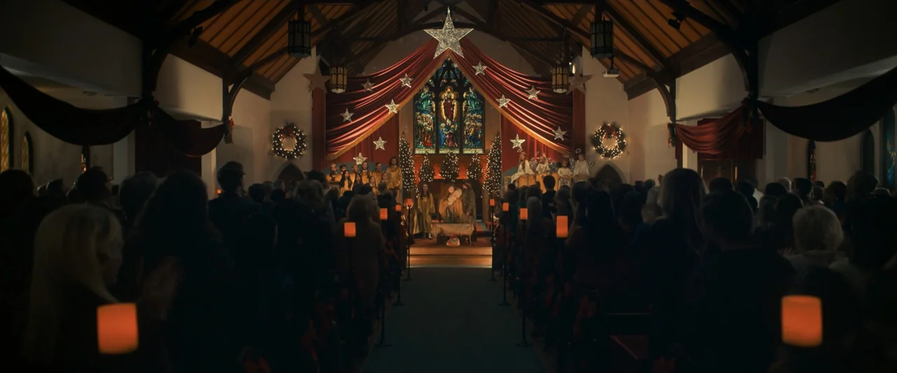 The Best Christmas Pageant Ever (2024) movie still: wide — A decorated church interior features a Christmas nativity scene staged on a raised…