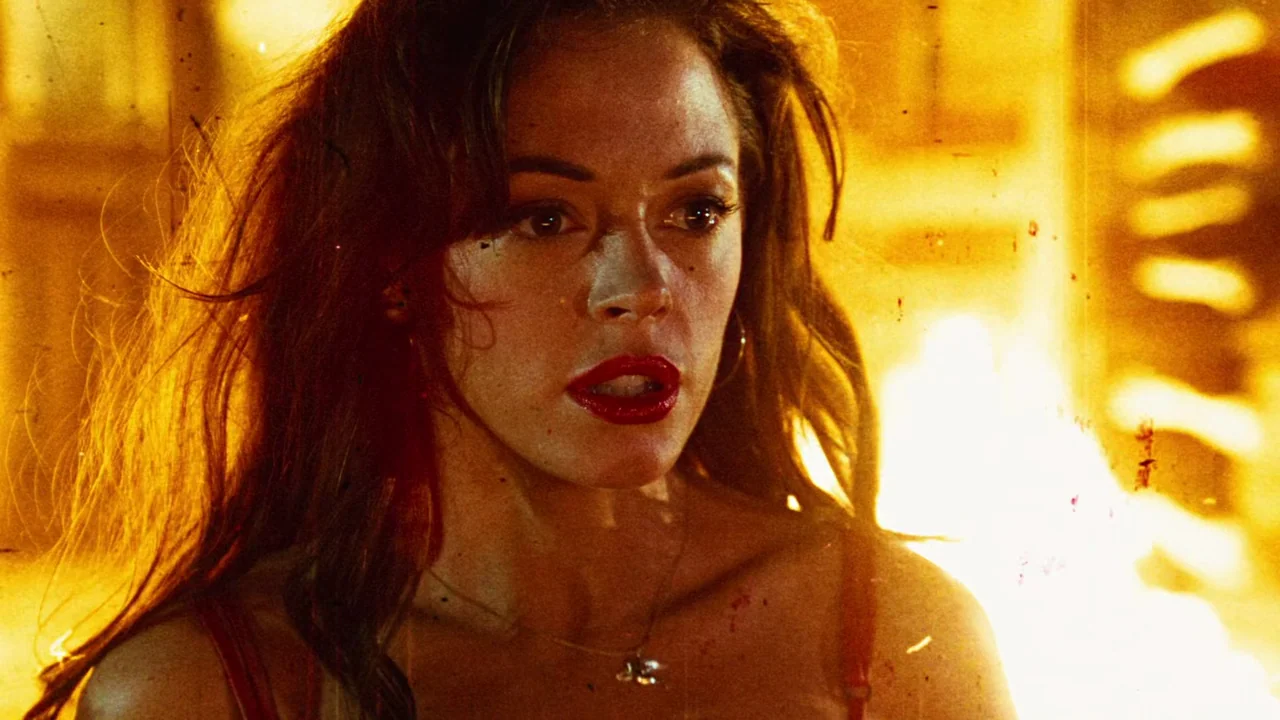 Planet Terror (2007) movie still: closeup — A woman stands in front of a raging fire during the night. The intense orange light casts deep shadows…