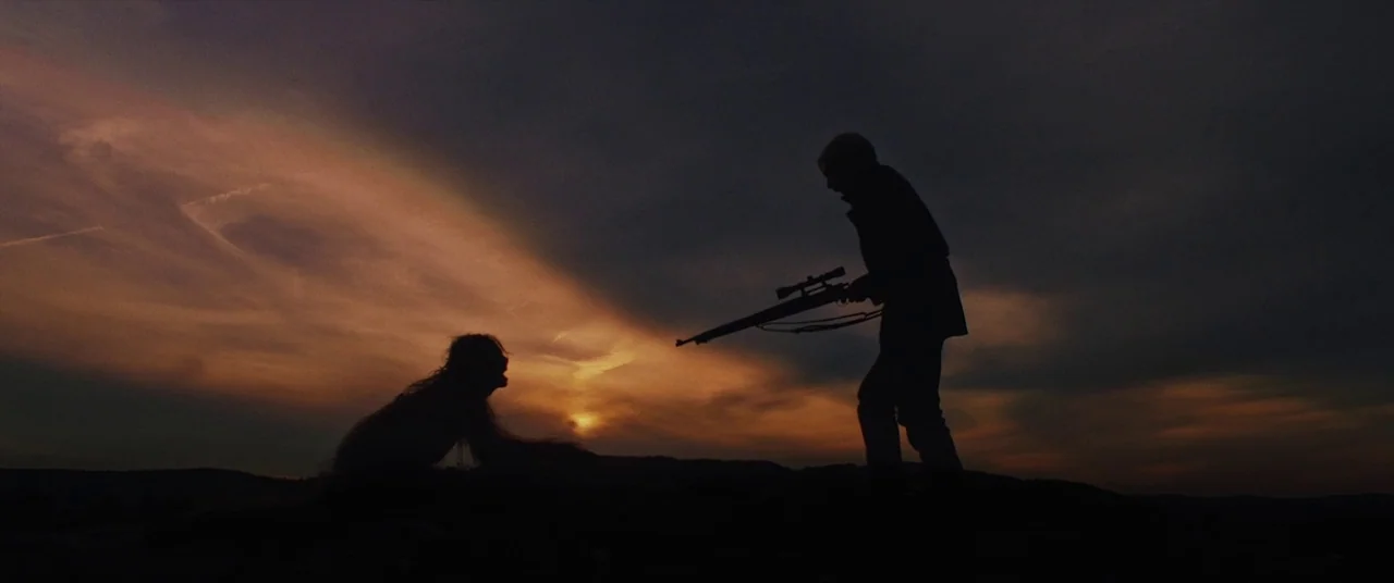 The Man Who Killed Hitler and Then the Bigfoot (2018) movie still: wide — An open desert landscape at dusk with a dark cloudy horizon. One person…