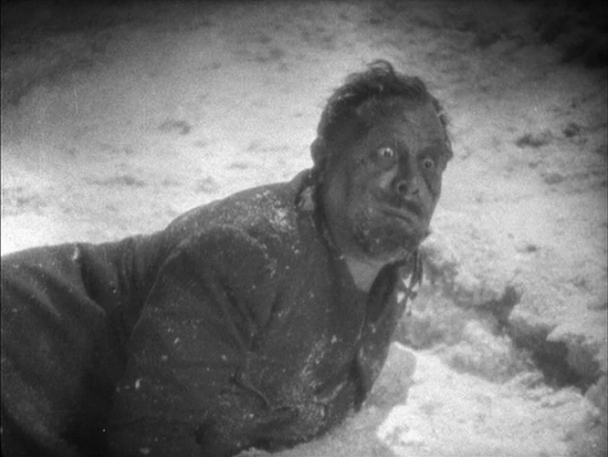 The Last Command (1928) movie still: medium — A man lies prone in a field covered in thick layers of snow. He is wearing a dark military coat and…