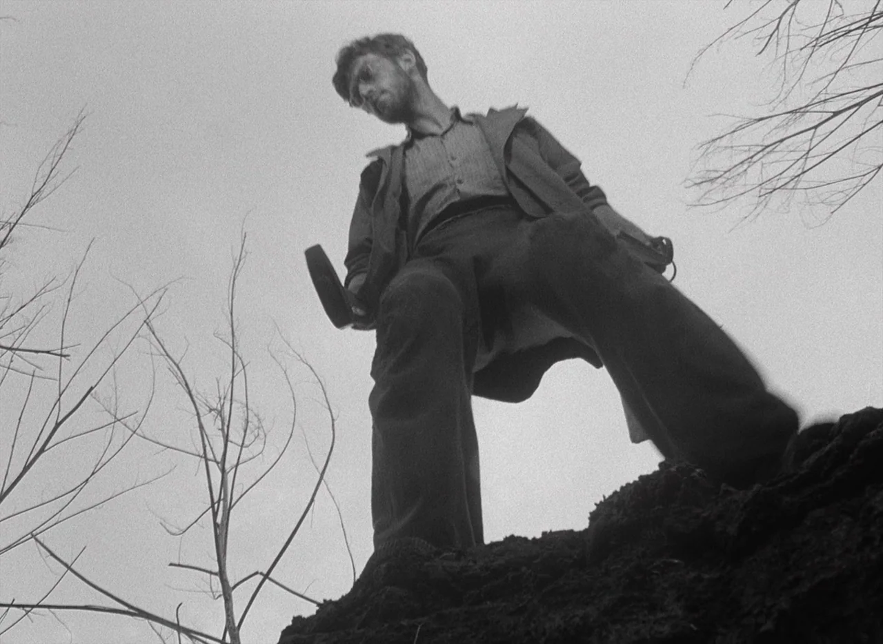 Letter Never Sent (1960) movie still: fullbody — An outdoor field under an overcast sky with bare, leafless trees at the edges. A man stands on a…