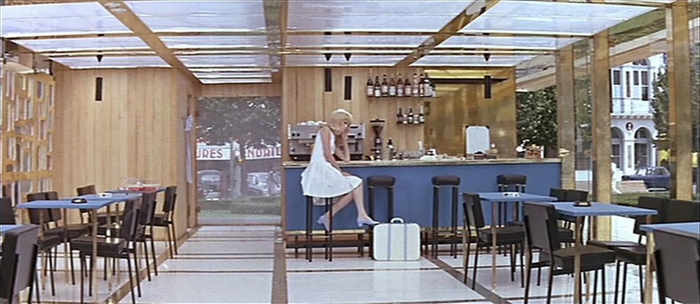 Les Demoiselles de Rochefort (1967) movie still: wide — A modern, minimalist cafe features wood-paneled walls, a blue bar, and gold framework. A…