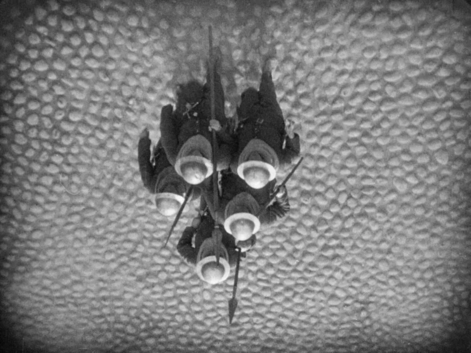 The Passion of Joan of Arc (1928) movie still: wide — A group of soldiers stands together on a cobblestone surface. They hold rifles vertically…