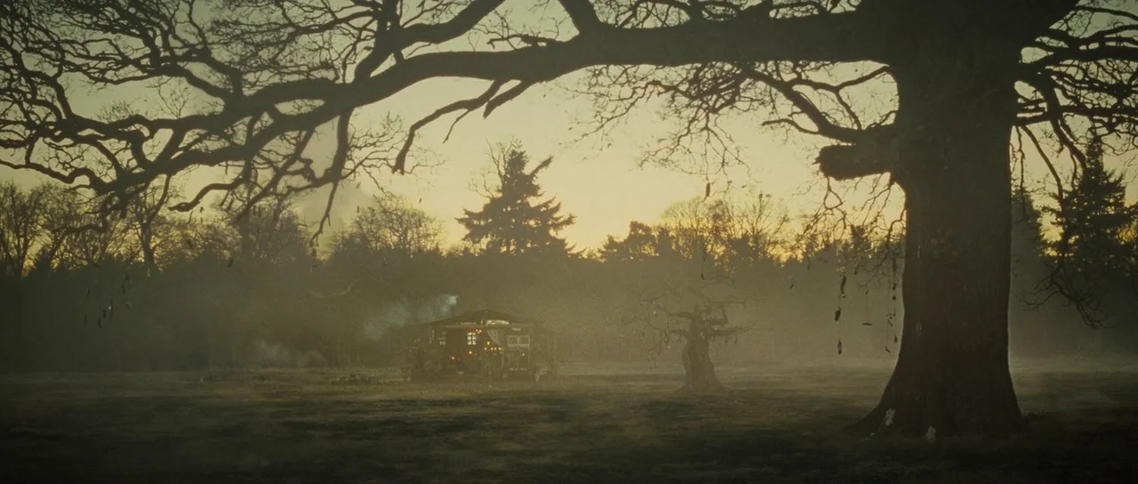 The World’s End (2013) movie still: establishing — A misty meadow features a small wooden shack surrounded by large mature oak trees. Smoke rises…