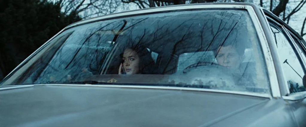 Wind Chill (2007) movie still: medium — Two people sit inside a car while viewed through a rain-streaked windshield. The woman speaks into a mobile…