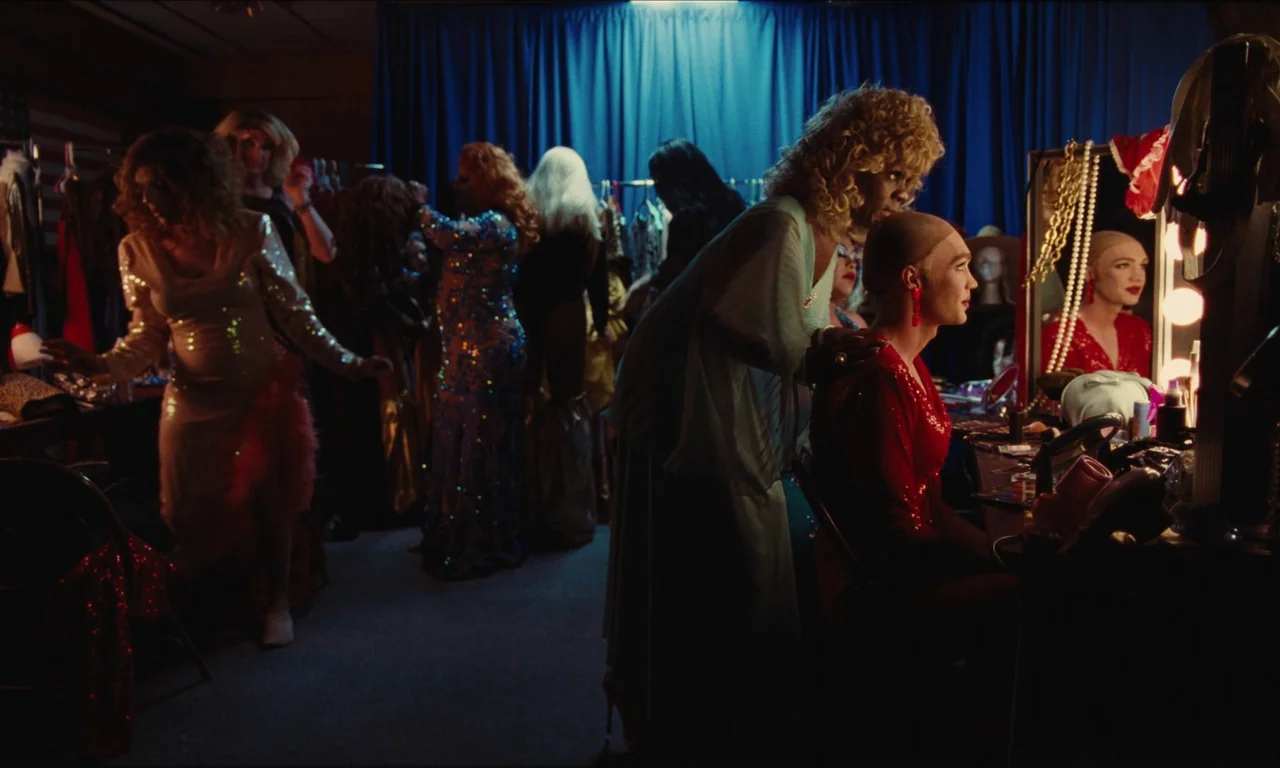 National Anthem (2023) movie still: medium — A crowded dressing room with blue curtains and racks of costumes visible in back. A person with a wig…