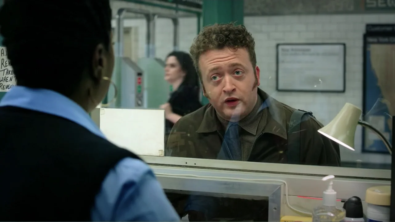 Ghostbusters (2016) movie still: medium — An interior information booth features a glass partition separating two people in a transit station. A man…