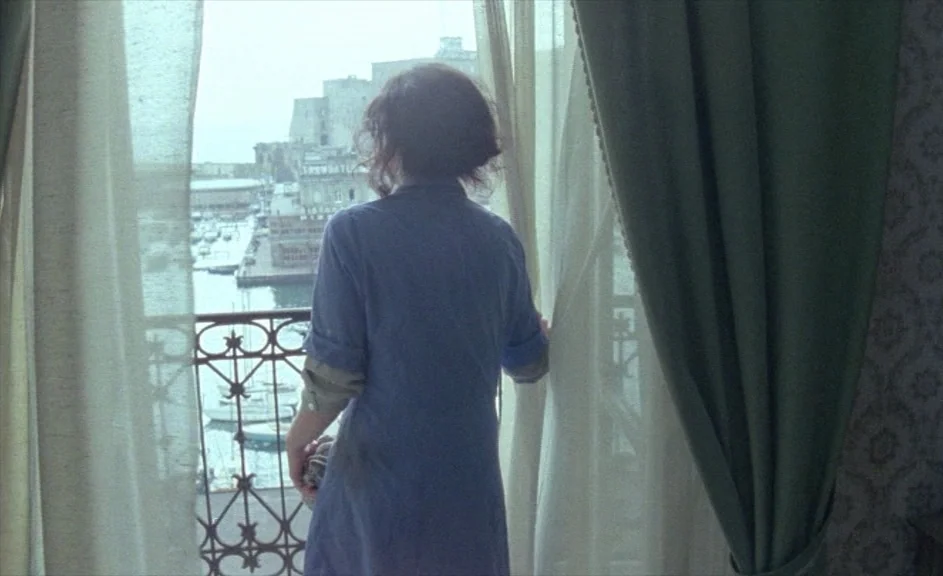 The Kingdom of Naples (1978) movie still: medium — A room with sheer white curtains overlooks a harbor viewed through an open balcony door. The…
