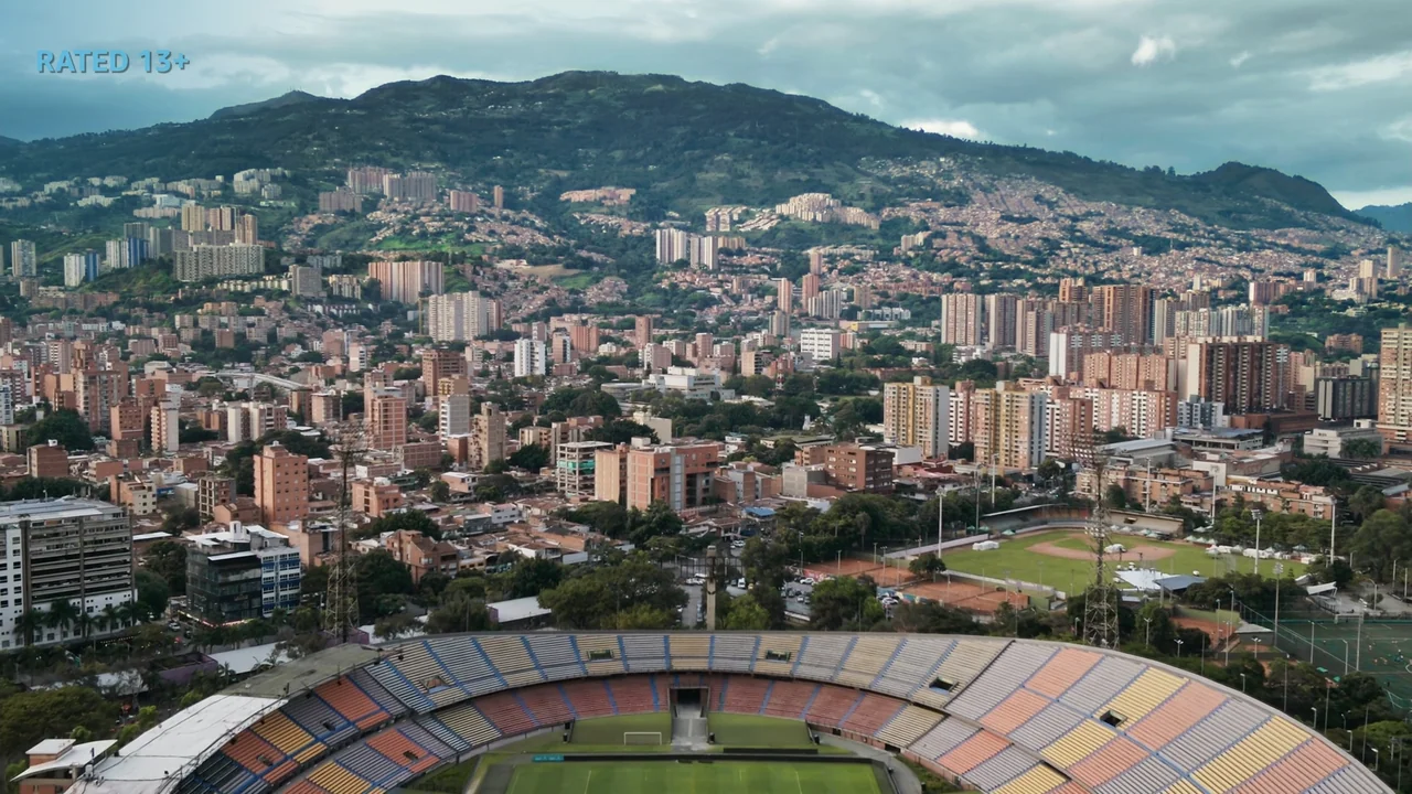An Affair: A Dangerous Sexual Play (2014) movie still: establishing — A high-angle aerial view of a large outdoor stadium with multi-colored seating…