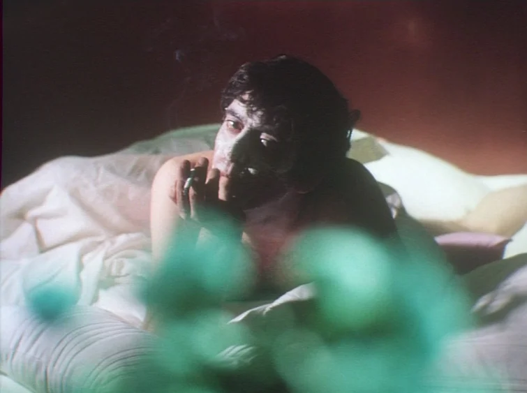 Hermitage (1968) movie still: medium — A man with a face mask lies shirtless in bed inside a dark room. He holds a lit cigarette between his fingers…