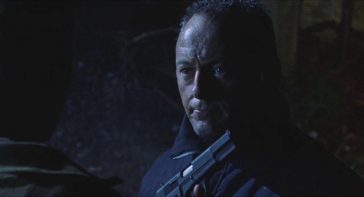 Dog Soldiers (2002) movie still: closeup — A dark outdoor space at night with limited ambient illumination from above. A man with a short haircut…