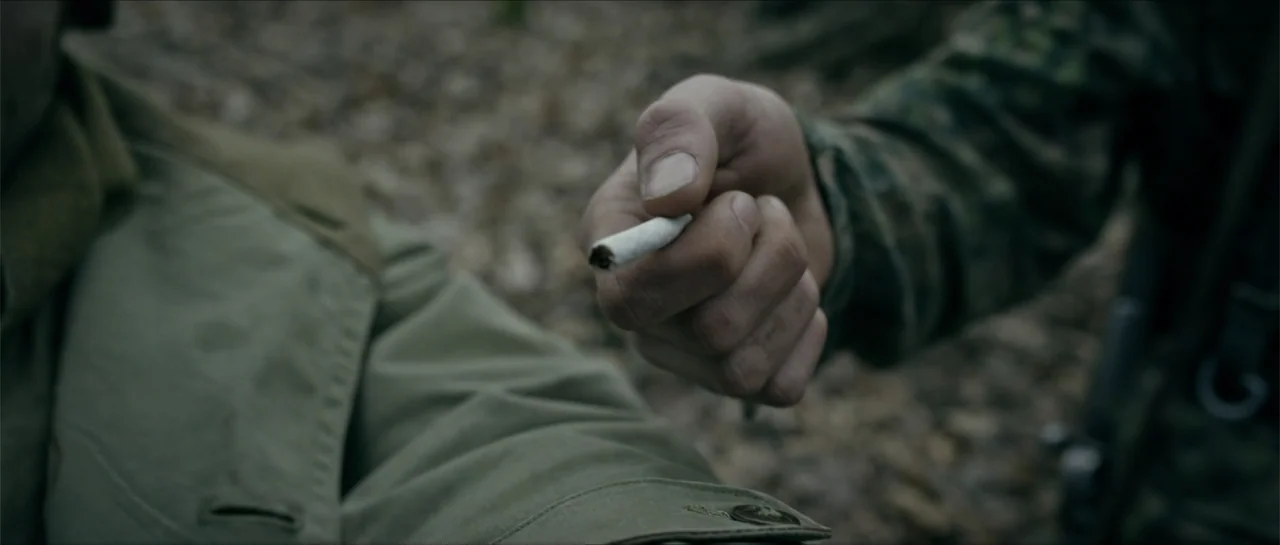 Battle of the Bulge (1965) movie still: closeup — An outdoor forest setting features dry leaves and foliage on the ground. A hand in camouflage…