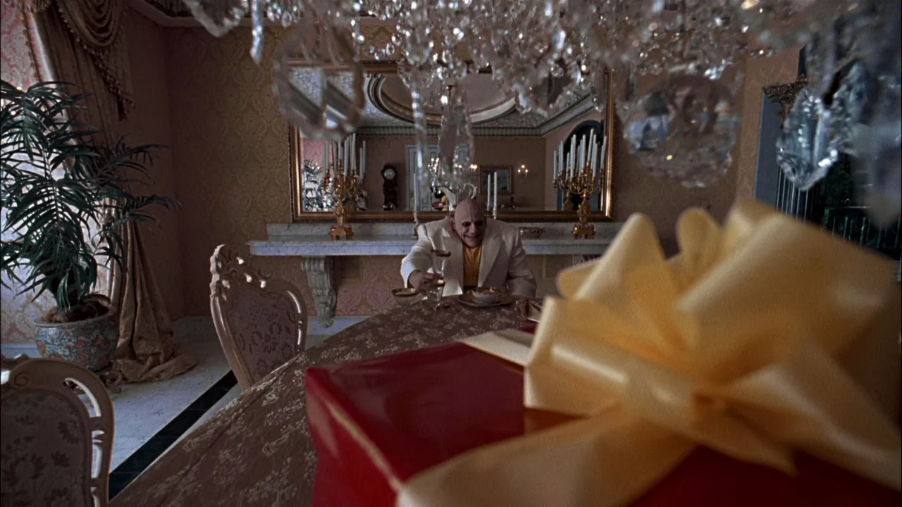 Addams Family Values (1993) movie still: medium — An opulent dining room features a large mirror, chandelier, and elaborate gold-patterned…