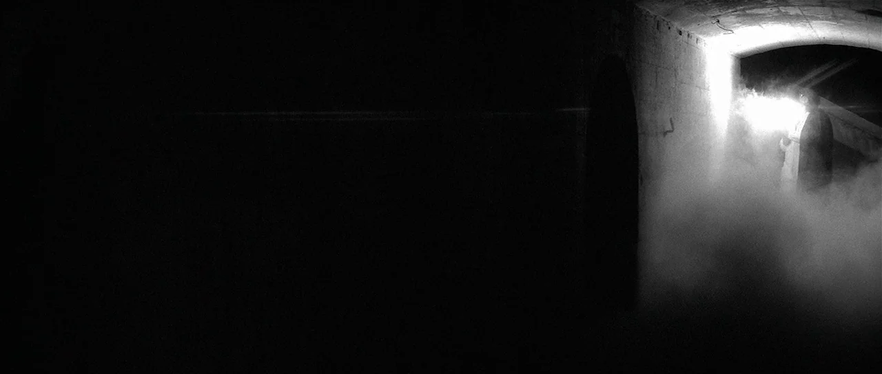The Last Battle (1983) movie still: wide — A dark, cavernous space features a stone archway filled with dense white smoke. A lone figure stands near…