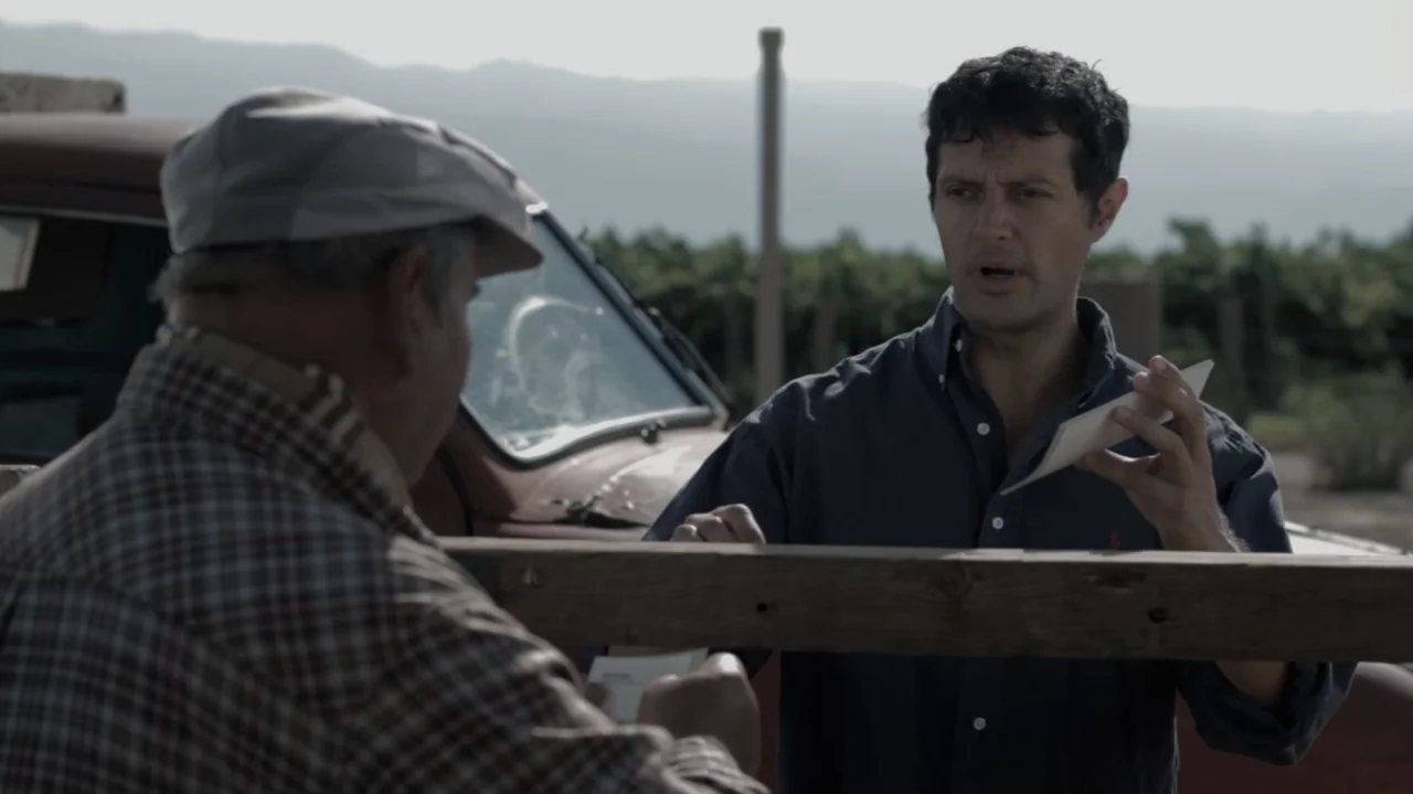 Still Life (2013) movie still: medium — A rural vineyard area features a vintage truck parked near a wooden gate. Two men stand on opposite sides of…