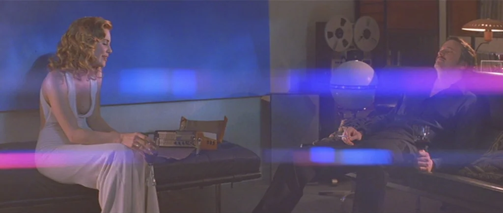 Where The Truth Lies (2005) movie still: medium — A dimly lit room features a pair of leather benches and retro recording equipment. A woman and a…