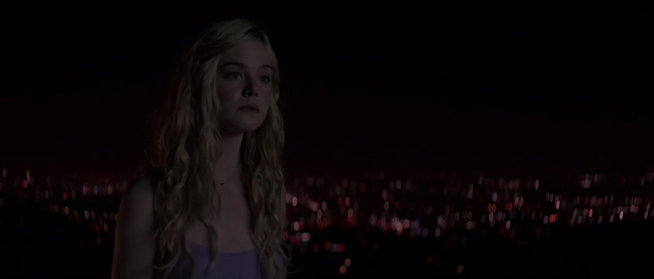 The Neon Demon (2016) movie still: medium — A young woman stands at a high vantage point overlooking an expansive, darkened cityscape at night.…