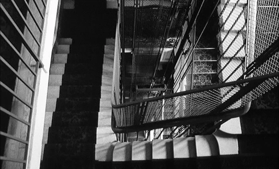 Boy Meets Girl (1984) movie still: establishing — An interior stairwell features geometric metal mesh railings and patterned carpeted stairs. The…