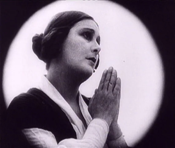 Destiny (1921) movie still: closeup — A close-up shot captures a woman in a dark dress with a white collar. She holds her hands together in a prayer…