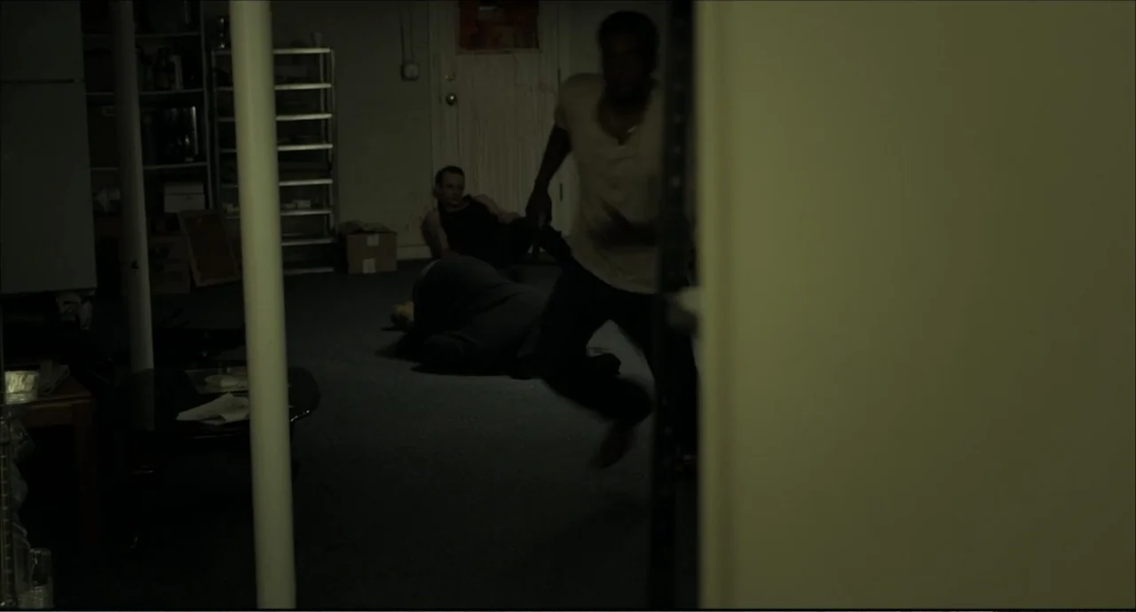 Freedom (2024) movie still: medium — A dark, cluttered basement interior features scattered furniture and a person running through frame. A man in a…
