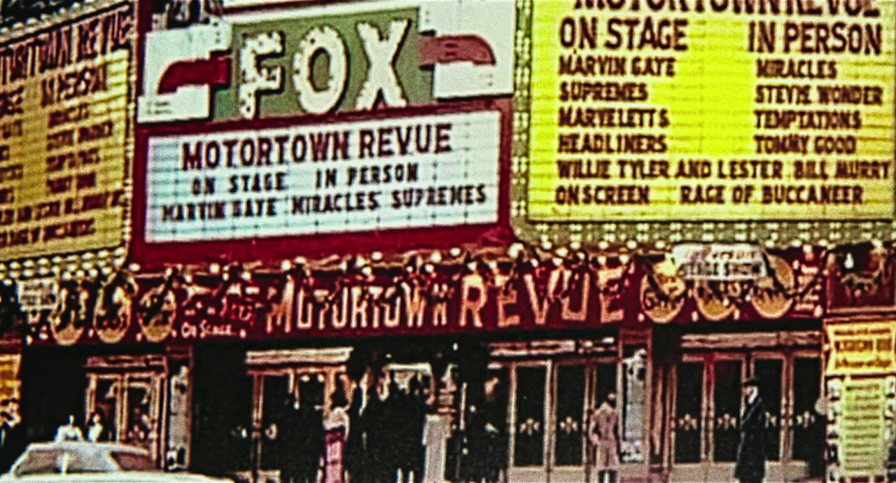 Detroit (2017) movie still: establishing — A vintage movie theater facade displays a Motortown Revue marquee in bright yellow and red. The entrance…