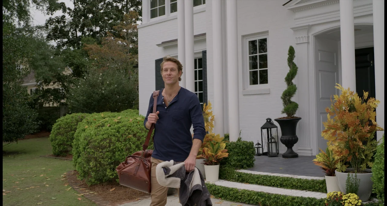 One True Loves (2023) movie still: medium — A white brick colonial-style house features columns at the entrance and lush green landscaping. A man…