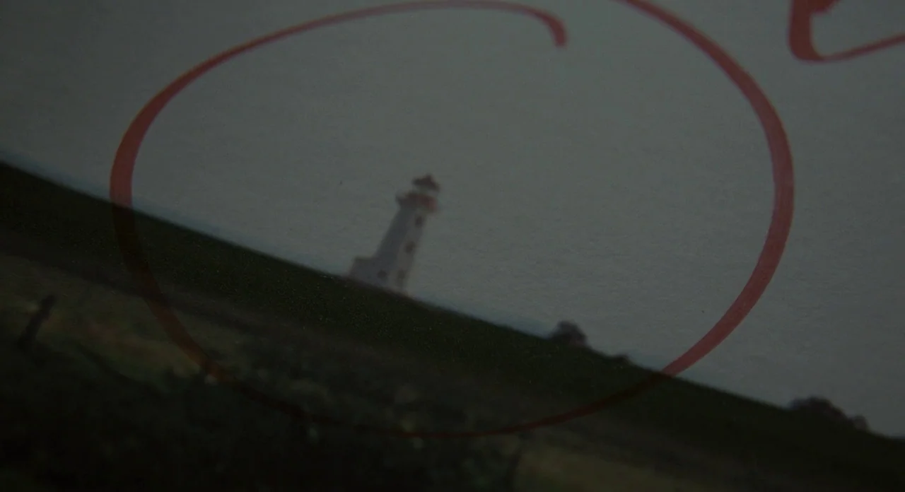 Promised Land (2012) movie still: establishing — A blurry photograph of a distant lighthouse sits on a surface. A red circular mark is drawn around…
