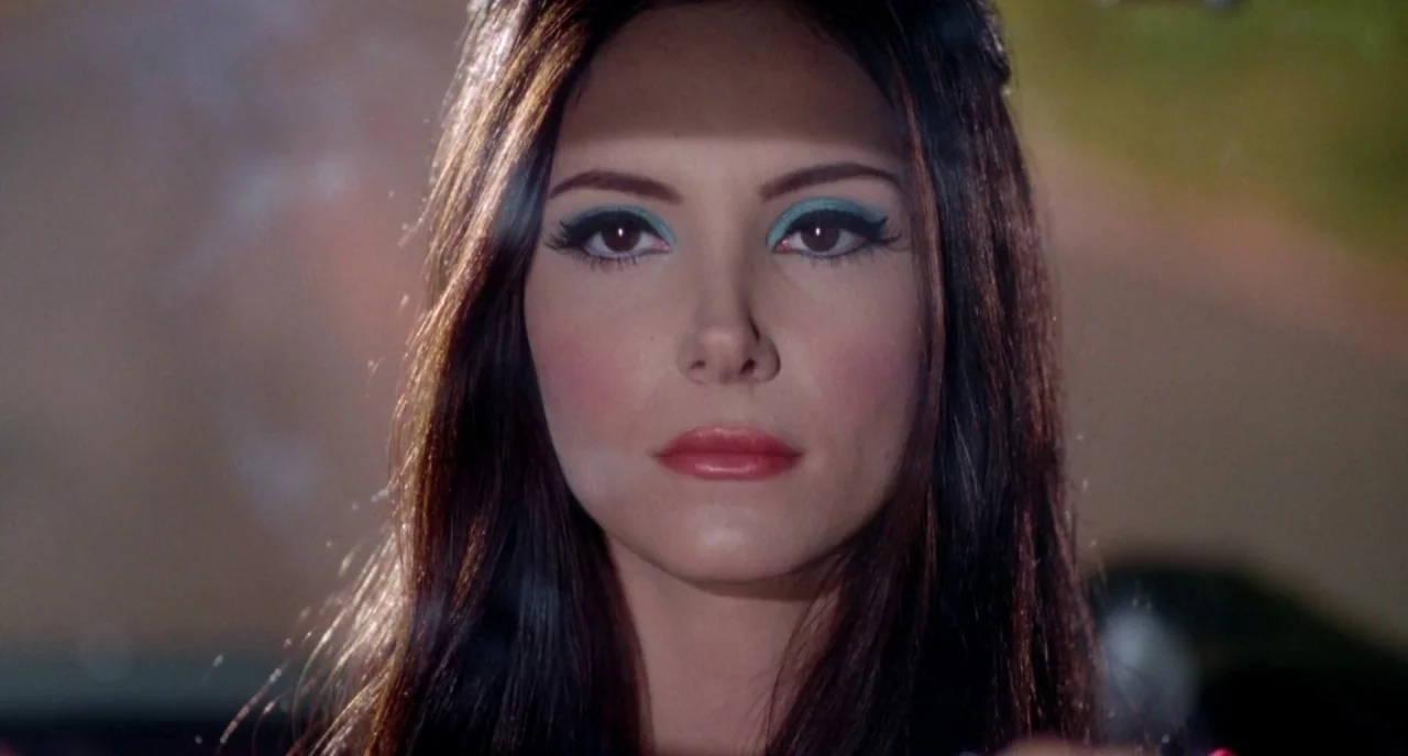 The Love Witch (2016) movie still: closeup — A woman sits inside a car during the day. The bright natural light illuminates her face while creating…