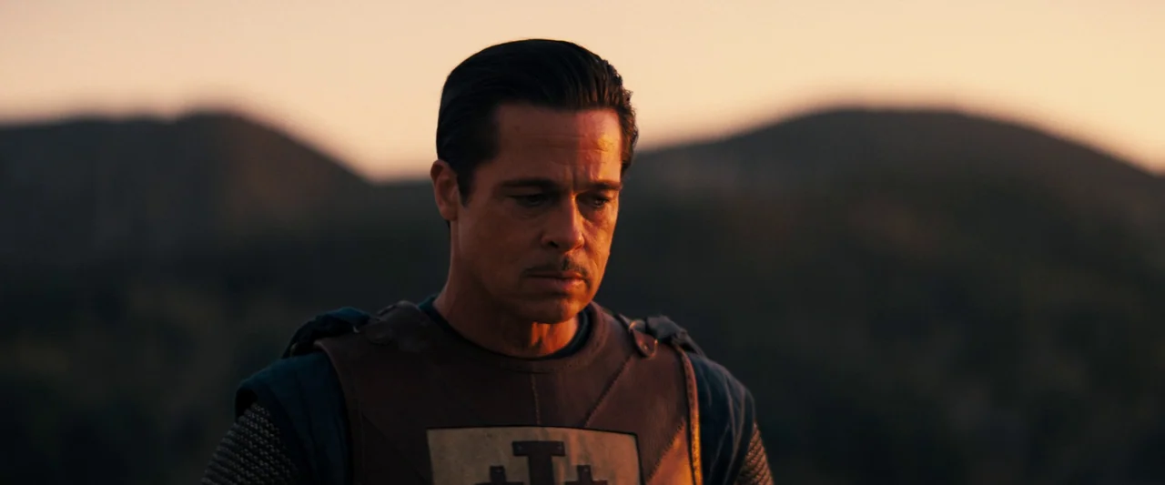 Babylon (2022) movie still: medium — A man wearing leather armor stands outside against a background of rolling hills. The late sun hits his face…
