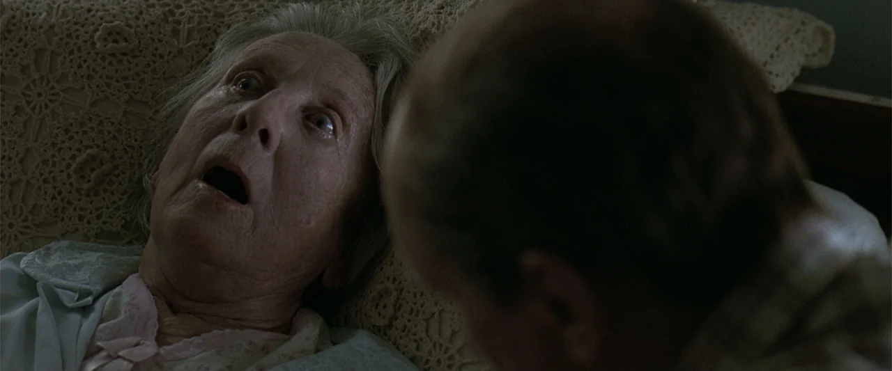 A Family Thing (1996) movie still: closeup — A dimly lit bedroom features an elderly woman lying on a crochet-covered pillow. A second person is…