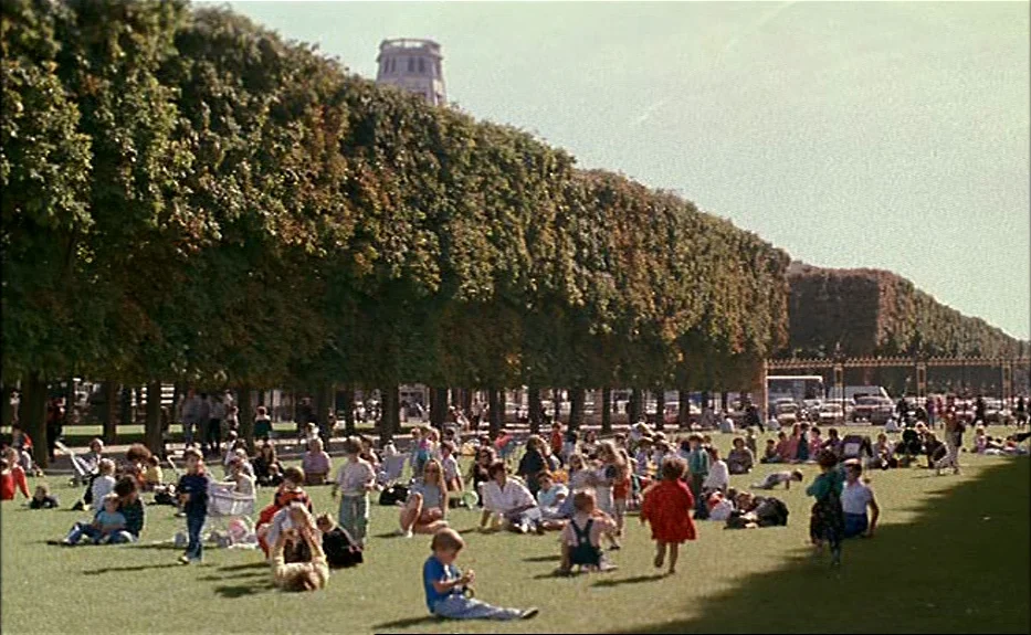 Les Amants Du Pont Neuf (The Lovers on the Bridge) (1991) movie still: wide — A crowded green park lawn is lined with rows of neatly trimmed dense…