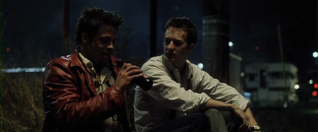 Fight Club (1999) movie still: medium — Two men sit on the ground in a dark, desolate industrial lot at night. A white trailer sits parked in the…
