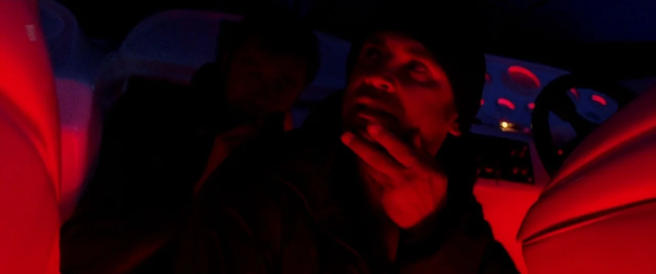 Bad Boys II (2003) movie still: medium — The interior of a vehicle at night is bathed in harsh red neon light. Two men sit together while one man…