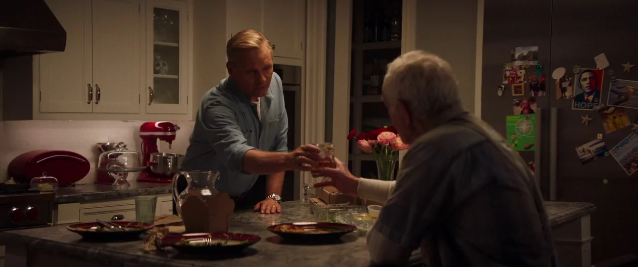 Falling (2020) movie still: medium — A modern white kitchen features a large marble-topped island with scattered food containers. Two men stand…