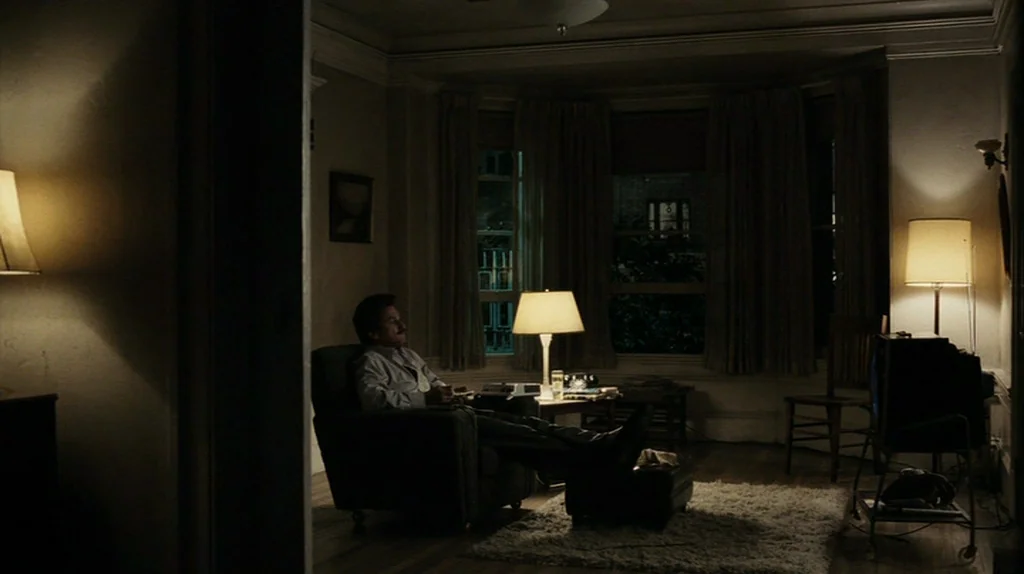 The Assassination of Richard Nixon (2004) movie still: wide — A dimly lit room with bay windows and vintage furniture arranged on a shaggy rug. A…