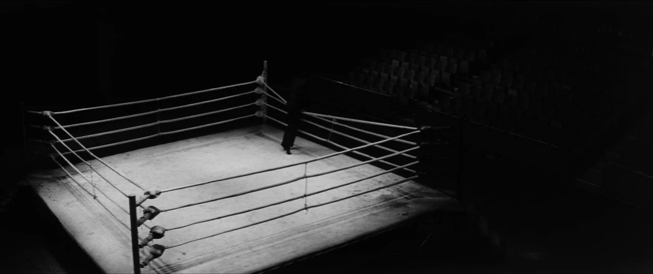 Branded To Kill (1967) movie still: wide — An empty boxing ring is illuminated by a sharp beam of light from above. The surrounding tiered seating…