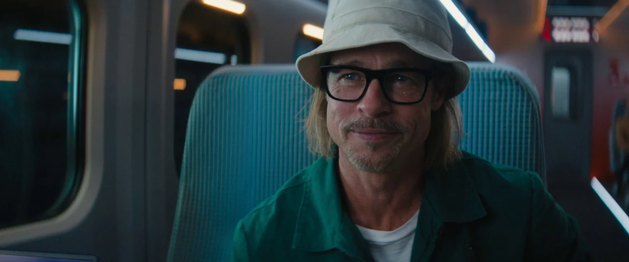 Bullet Train (2022) movie still: medium — A modern train car interior with ribbed blue-green fabric seat backs. A man sits in a seat, wearing…