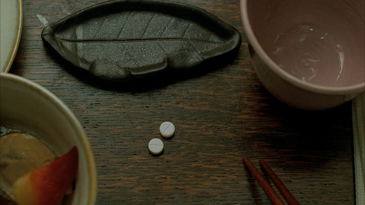 A Tale of Two Sisters (2003) movie still: closeup — A dark-stained wooden dining surface holds two ceramic bowls, a leaf-shaped dish, and…
