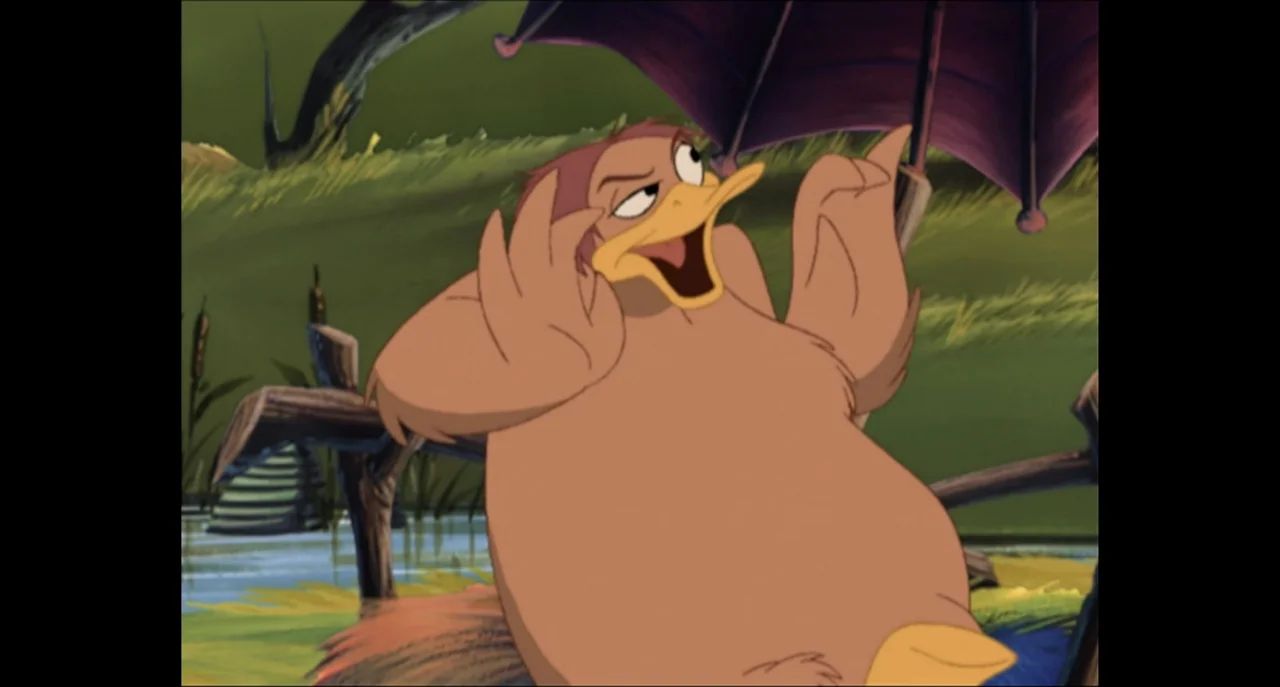 The Sissy Duckling (1999) movie still: medium — A cartoon wetland scene features grass and a wooden fence near a small pond. A brown anthropomorphic…