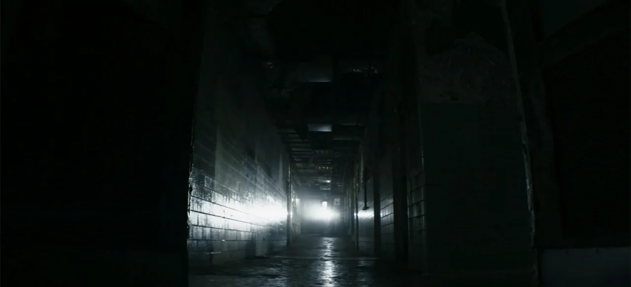 I Still See You (2018) movie still: wide — A dark, narrow industrial corridor features tiled walls and a recessed ceiling structure. A distant…