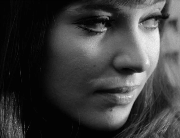 Alphaville (1965) movie still: closeup — A close-up of a young woman's face fills the frame against an blurred background. Her eyes gaze to the…