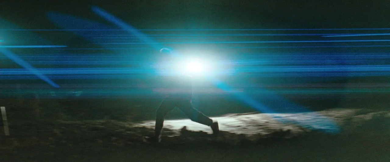The Adjuster (1991) movie still: wide — A dark, featureless expanse at night with a single bright light source. A solitary person runs across the…