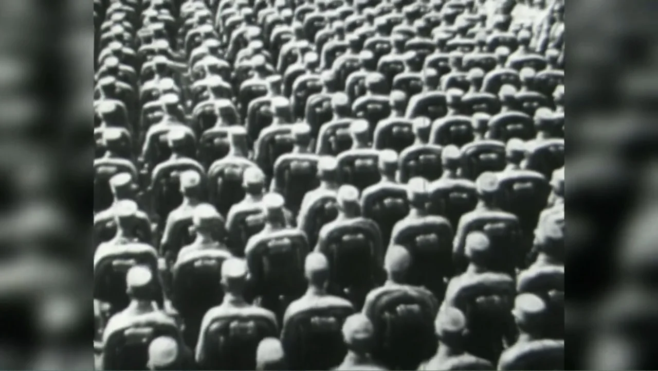 Almost Human: Rise of the Apes (2022) movie still: wide — A large outdoor space filled with a dense crowd of uniformed individuals. Rows of people…