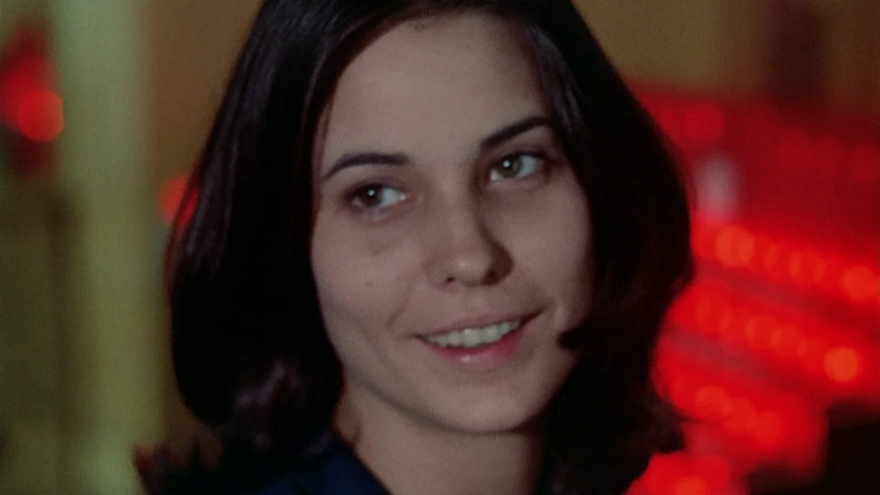 The Sentinel (1977) movie still: closeup — A close-up shot set in a dark room with blurred red light sources visible. A young woman with dark hair…