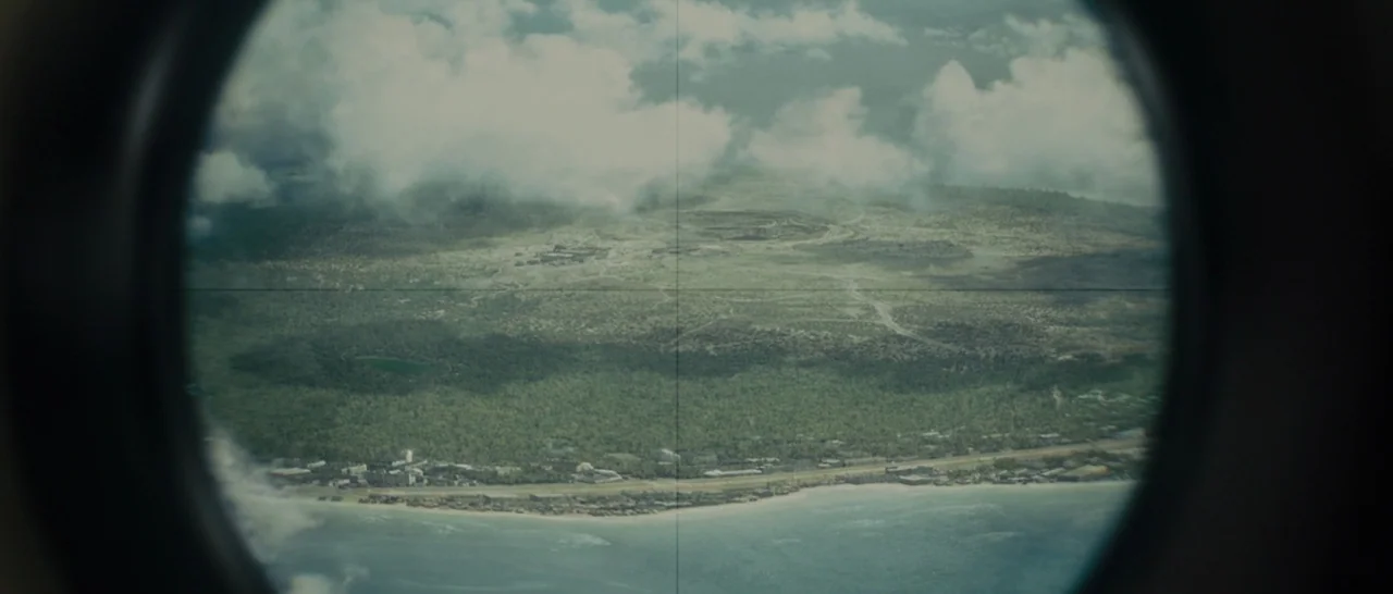 Unbroken (2014) movie still: establishing — A view through a circular optical device showing a tropical island with palm forests. White clouds cast…