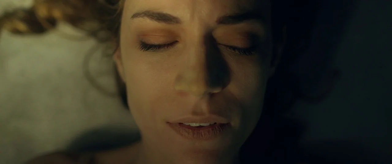 The Void (2016) movie still: closeup — The face of a woman is centered against a dark, indistinct background. She lies horizontally with her eyes…