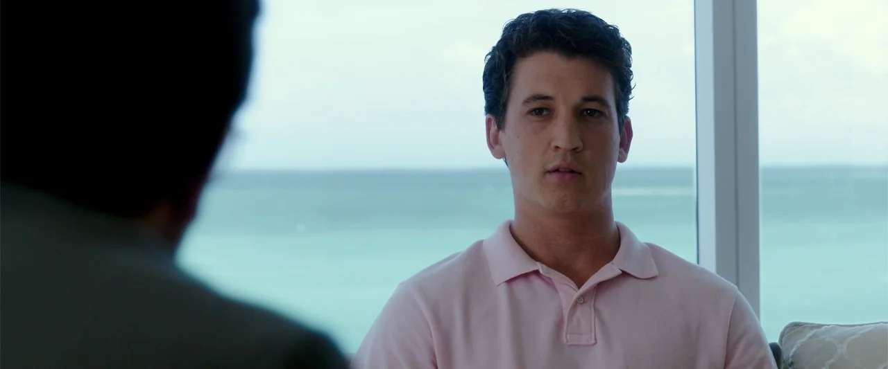 War Dogs (2016) movie still: medium — A room with a floor-to-ceiling glass wall overlooking a turquoise ocean. A man sits facing an unseen person in…