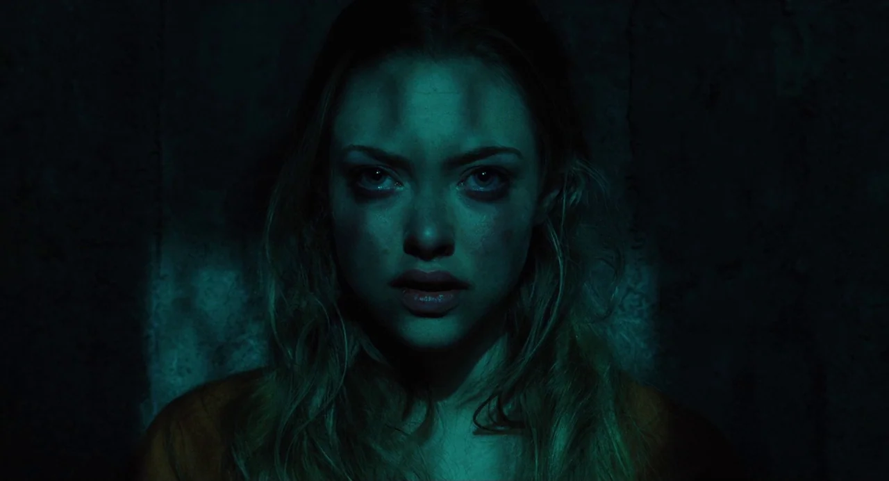 Jennifer’s Body (2009) movie still: closeup — A woman stands in a pitch-black, enclosed space with concrete-like textured walls. A singular, narrow…