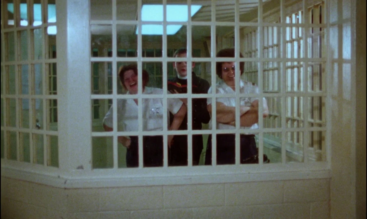Female Trouble (1974) movie still: medium — An interior space features a white grid window separating the foreground from three people. The three…