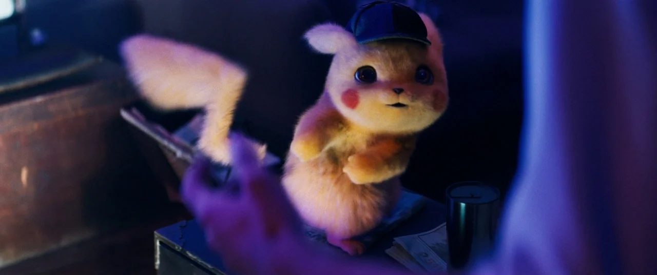 Pokémon Detective Pikachu movie still: medium — A dimly lit room contains a desk with various papers and a metallic cup. A small yellow creature…